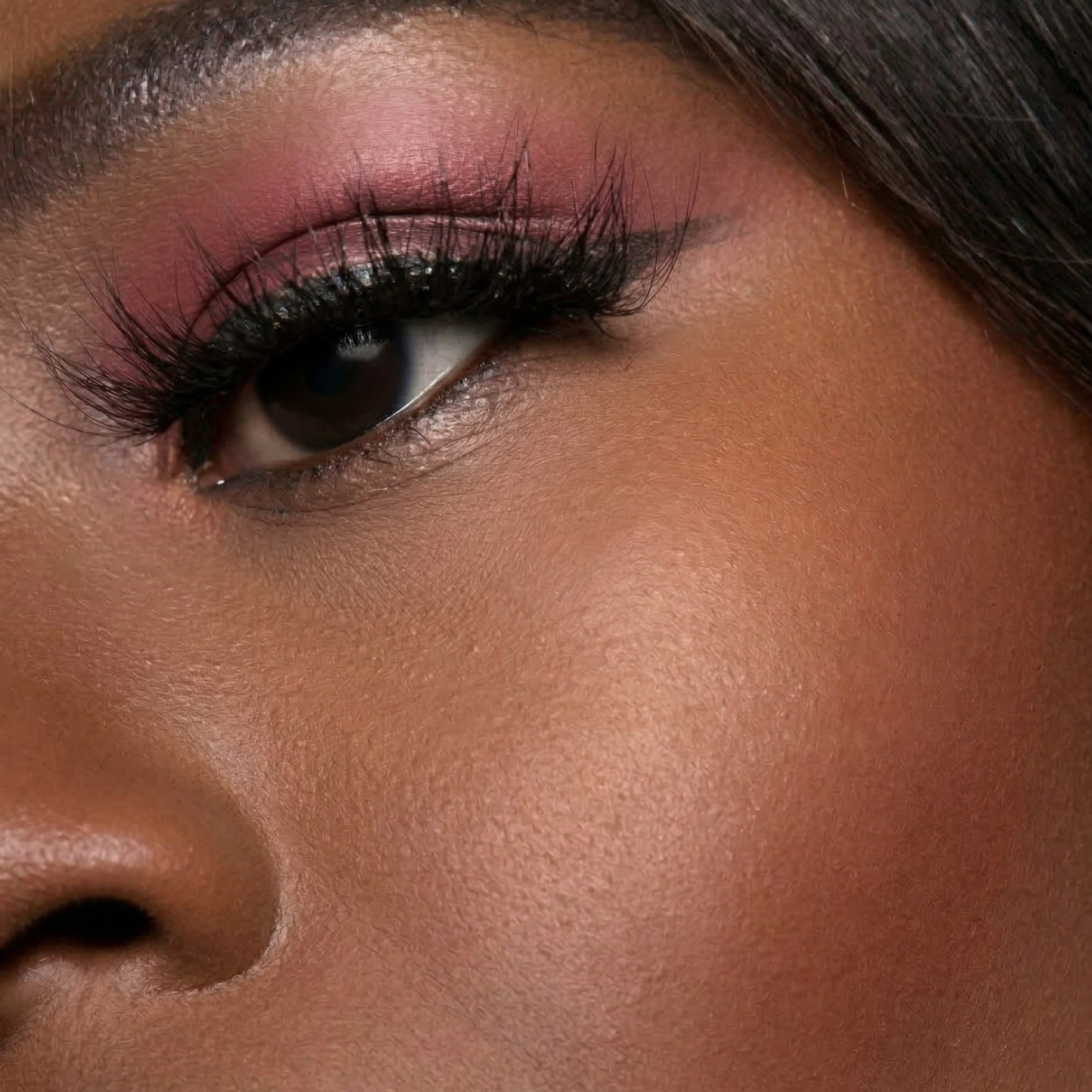 Close-up of a woman's eye with pink eyeshadow and long eyelashes.