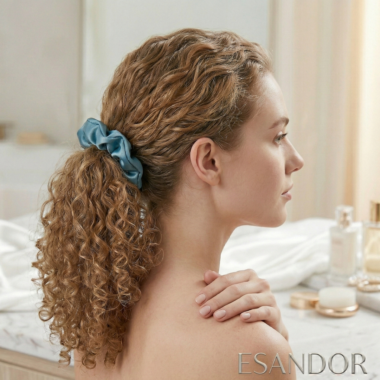 Woman with styled hair featuring a blue scrunchie, sitting in a spa-like setting with 'ESANDOR' branding.