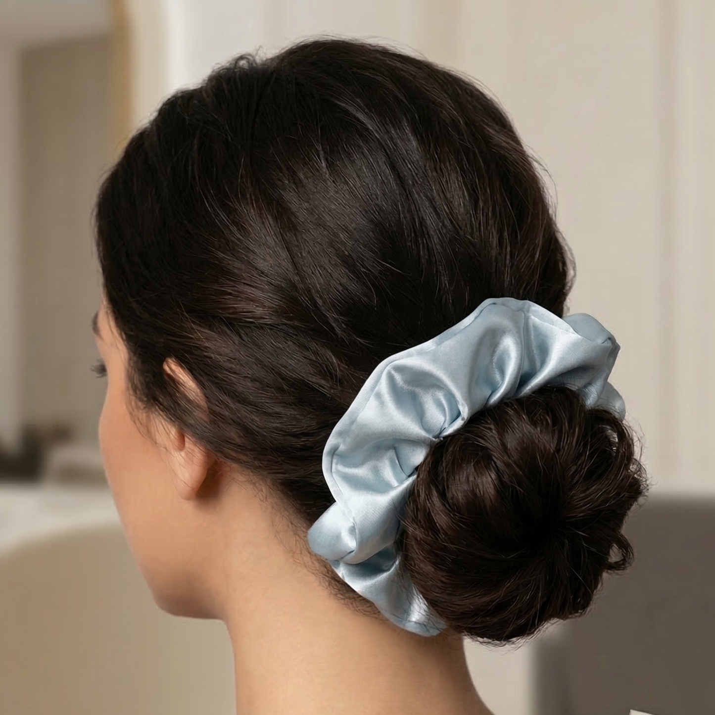 Woman with a blue satin scrunchie in her hair against a neutral background