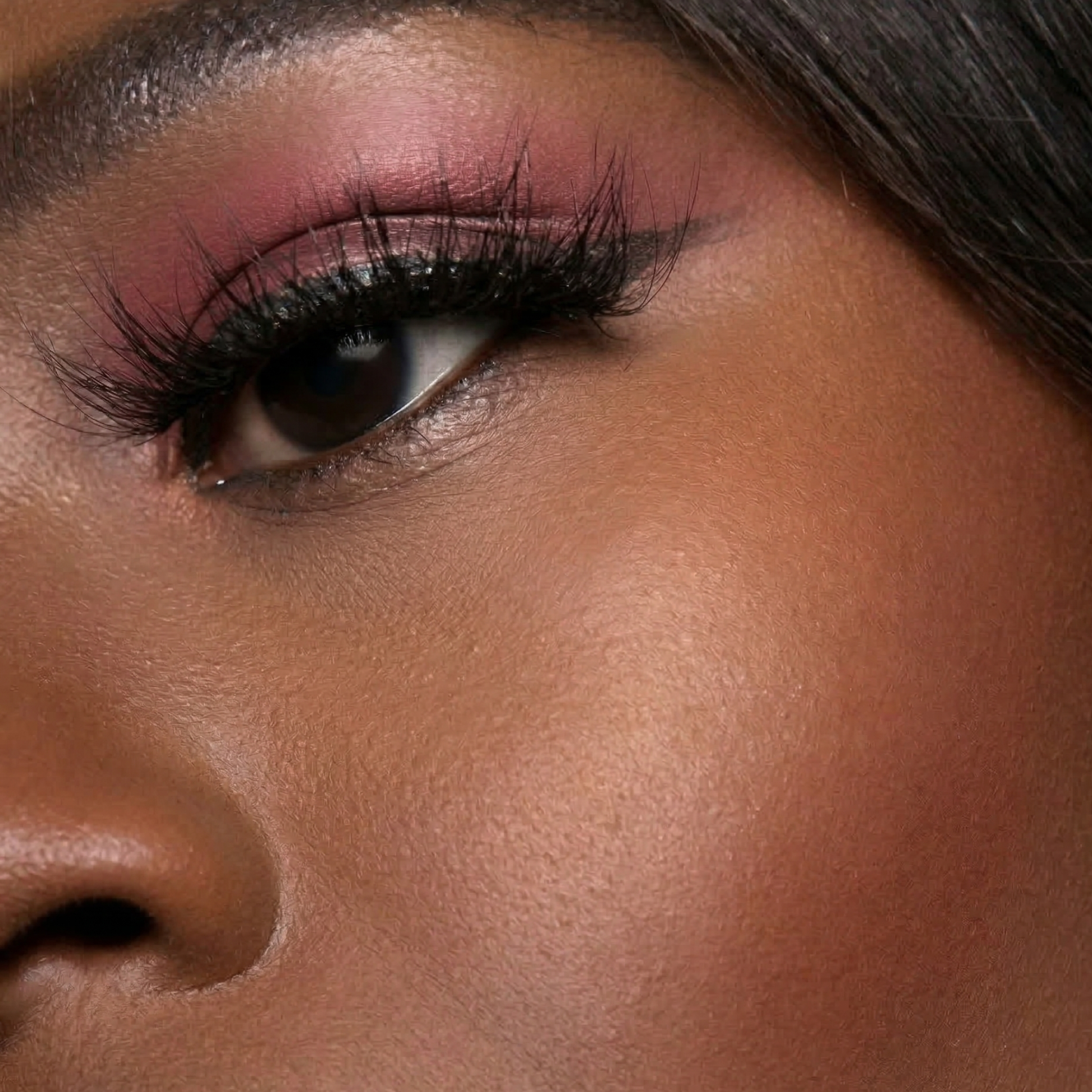Close-up of a woman's eye with pink eyeshadow and long eyelashes.