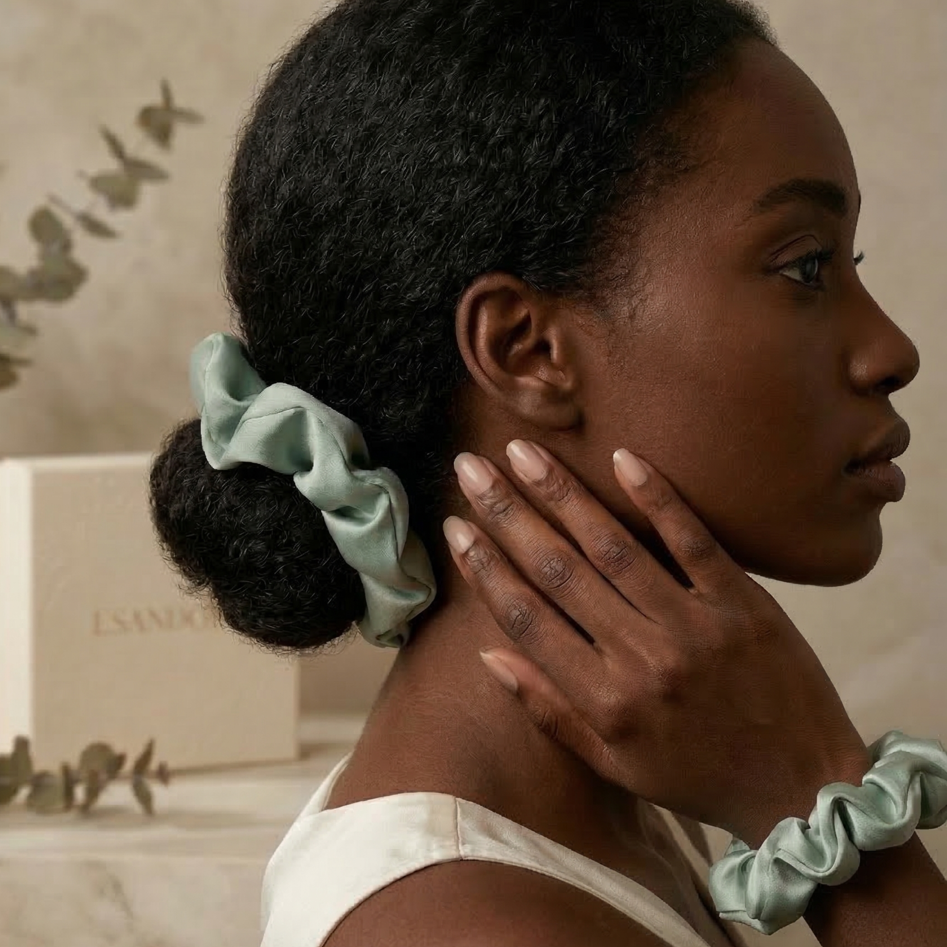 Woman with green scrunchie in hair and on wrist, with a neutral background