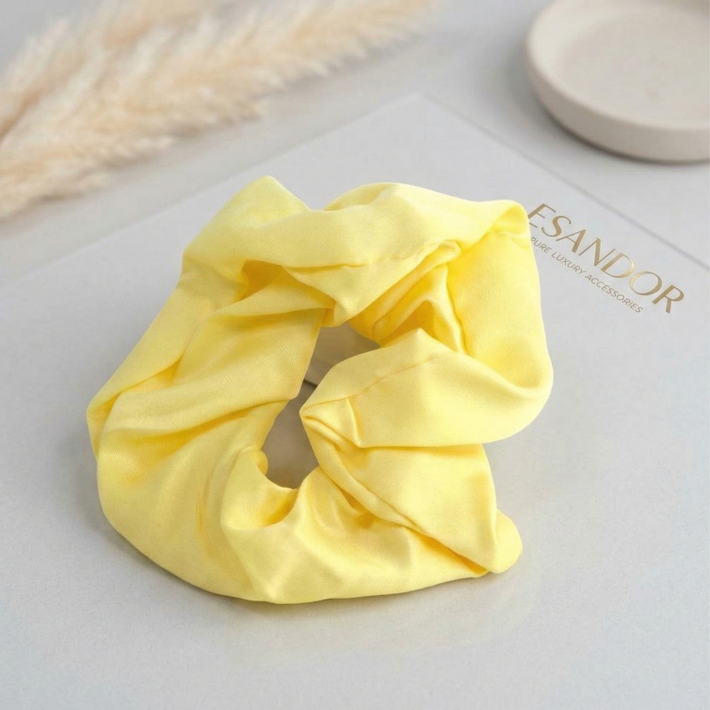 Yellow scrunchie on a light gray surface with 'ESANDOR' branding.