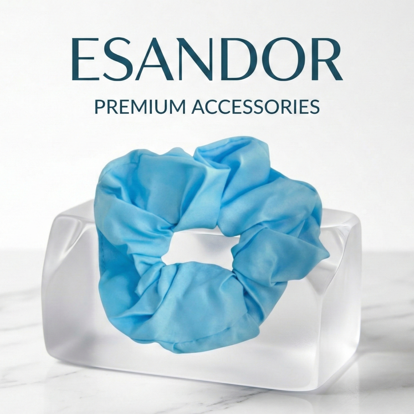 Blue scrunchie on a clear block with 'ESANDOR' branding above on a light background