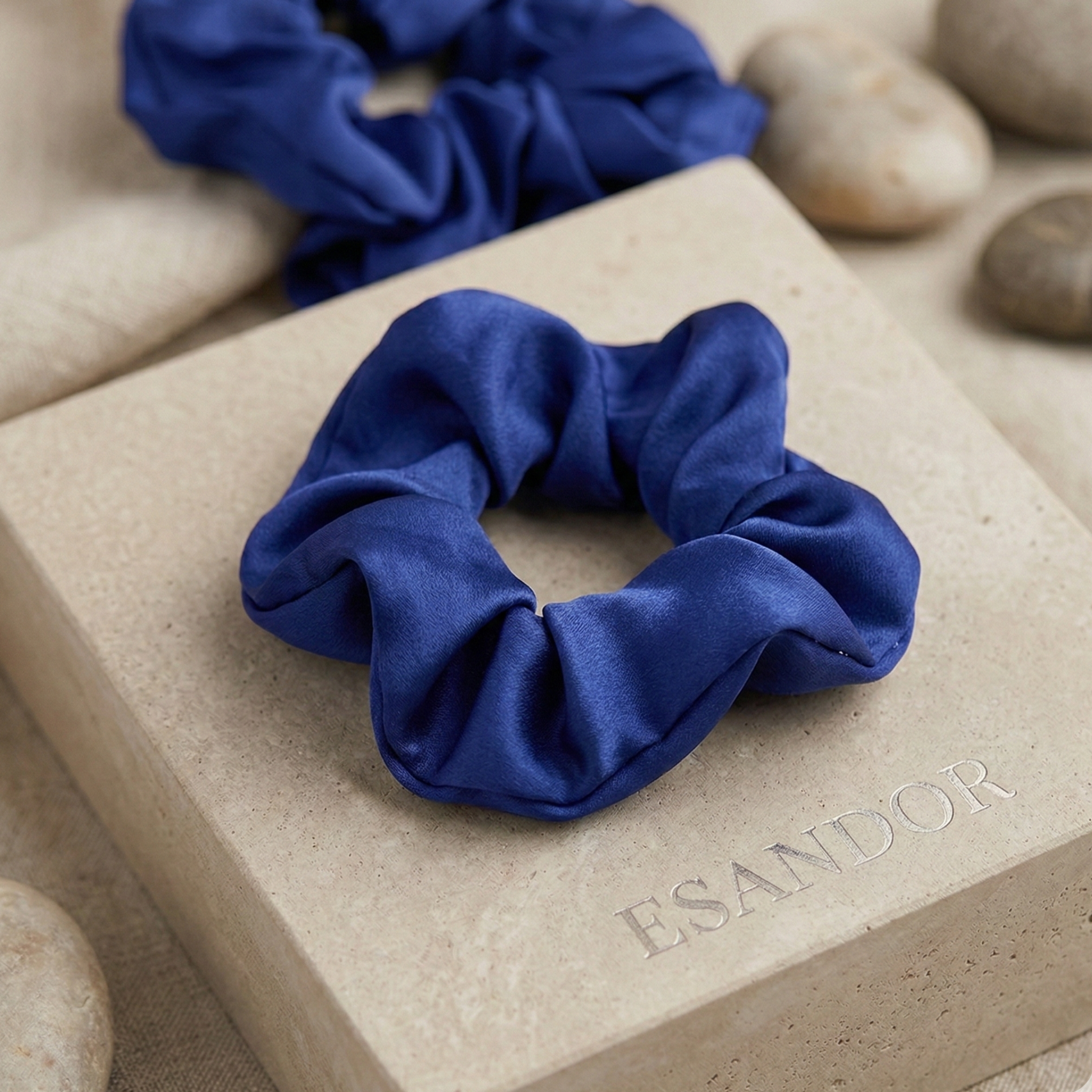 Blue scrunchie on a stone surface with 'ESANDOR' branding