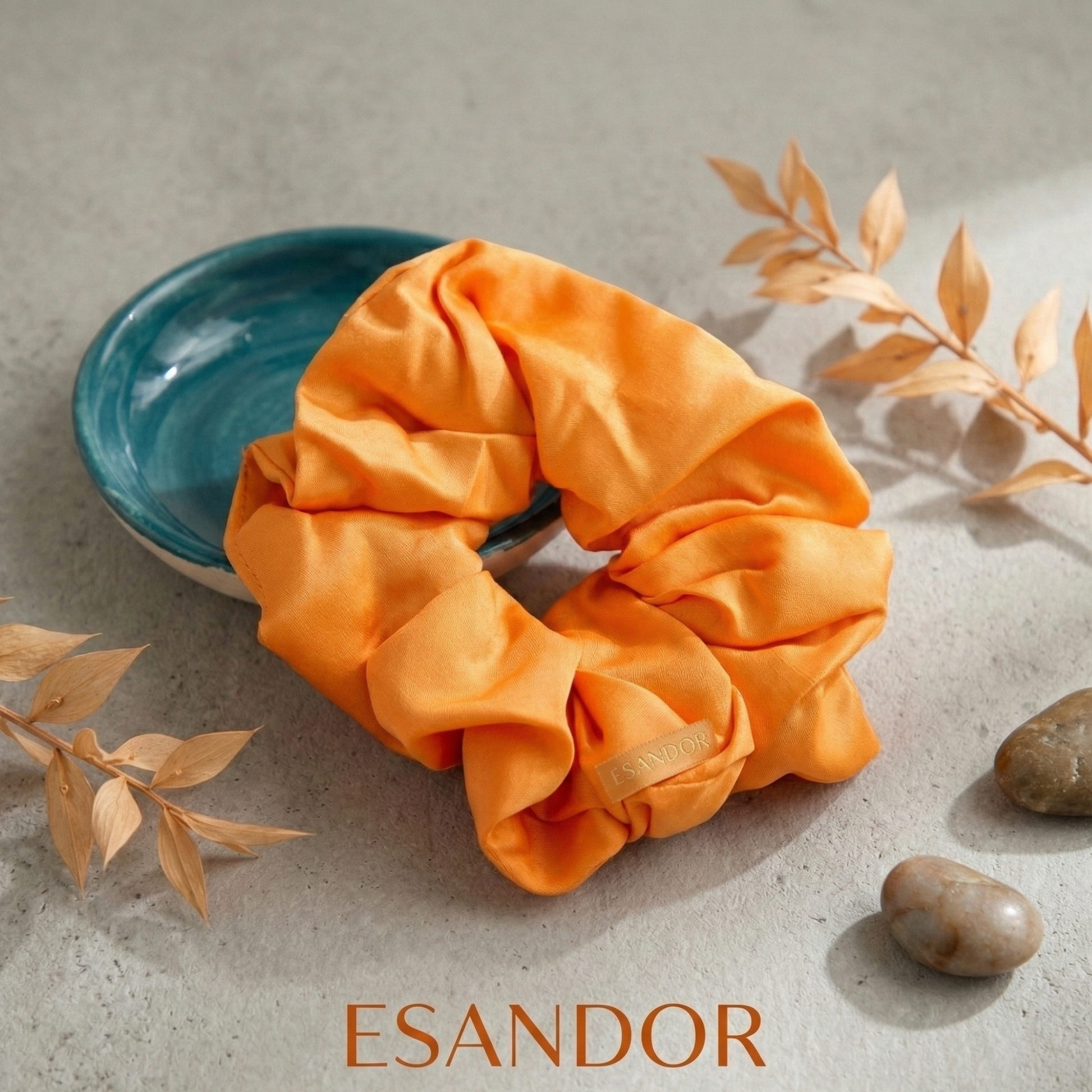Orange scrunchie on a textured surface with 'ESANDOR' branding.