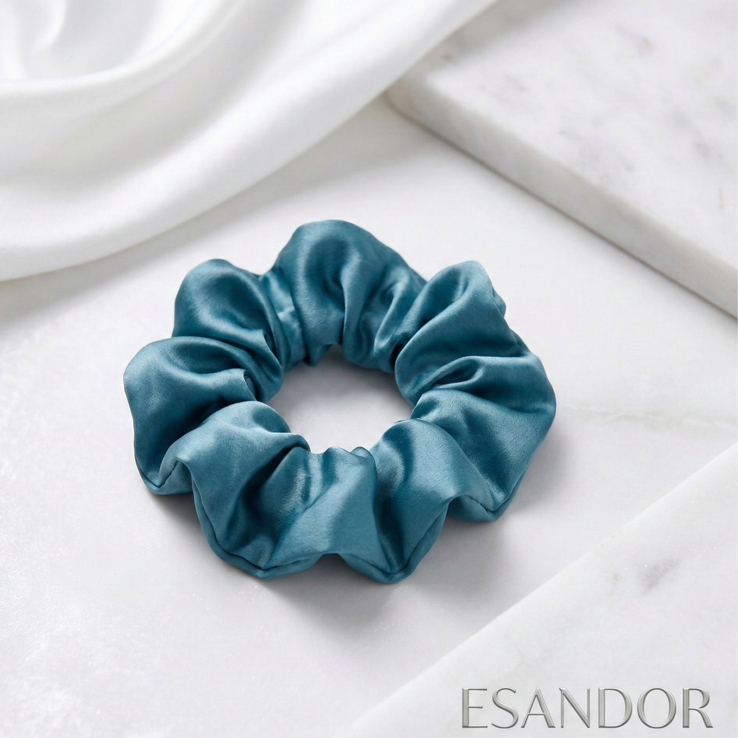 Blue scrunchie on a white fabric background with 'ESANDOR' branding.
