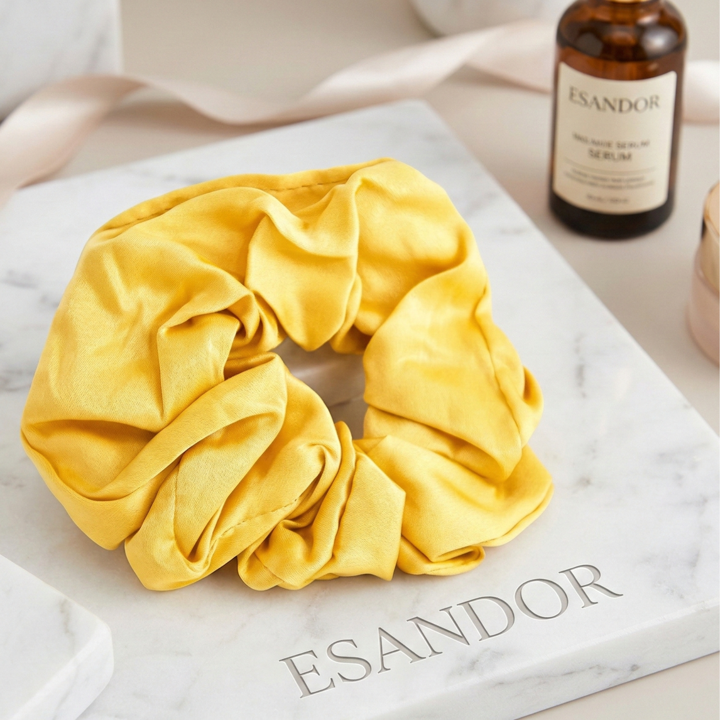 Yellow scrunchie on a marble surface with 'ESANDOR' branding.
