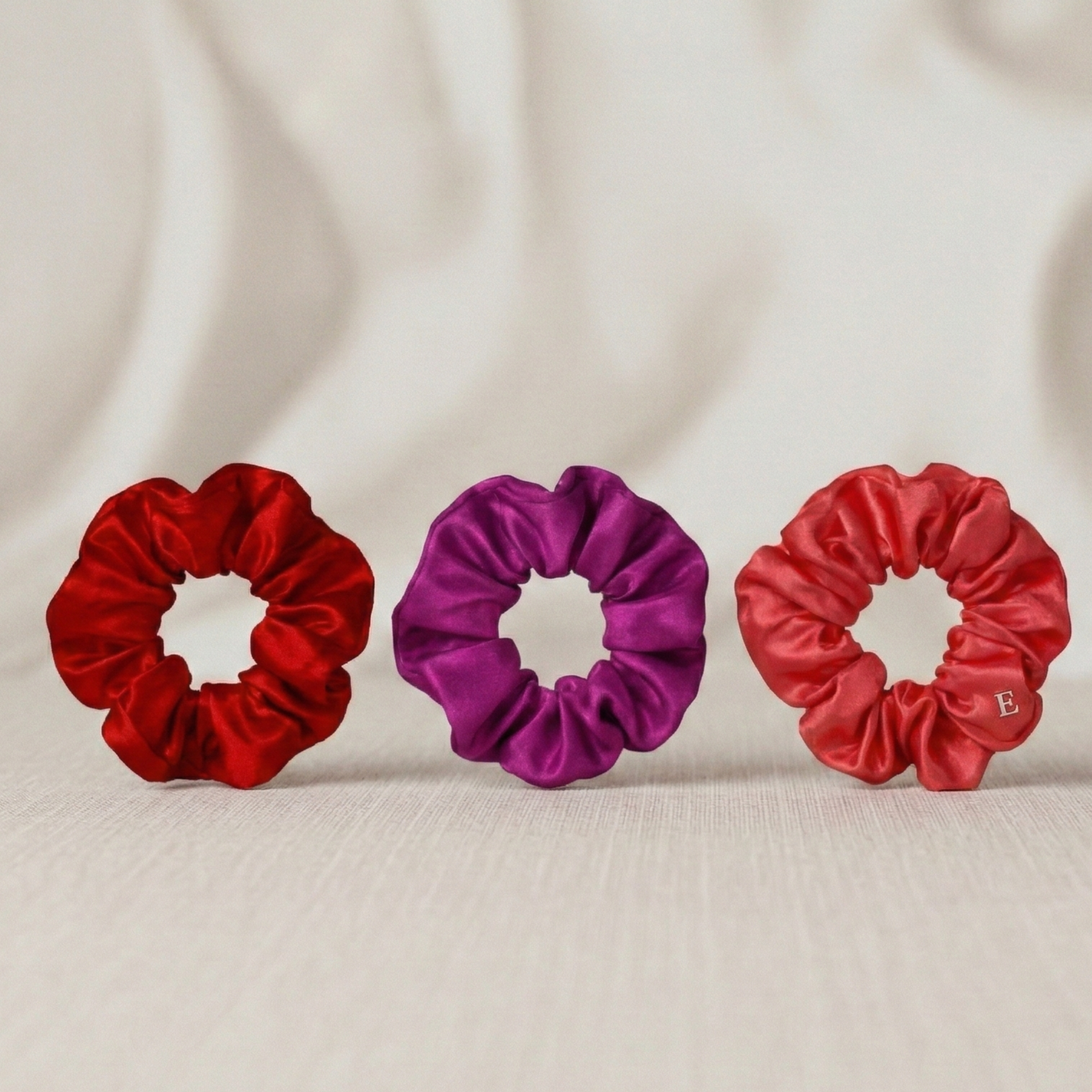 Three scrunchies in red and purple on a beige fabric background