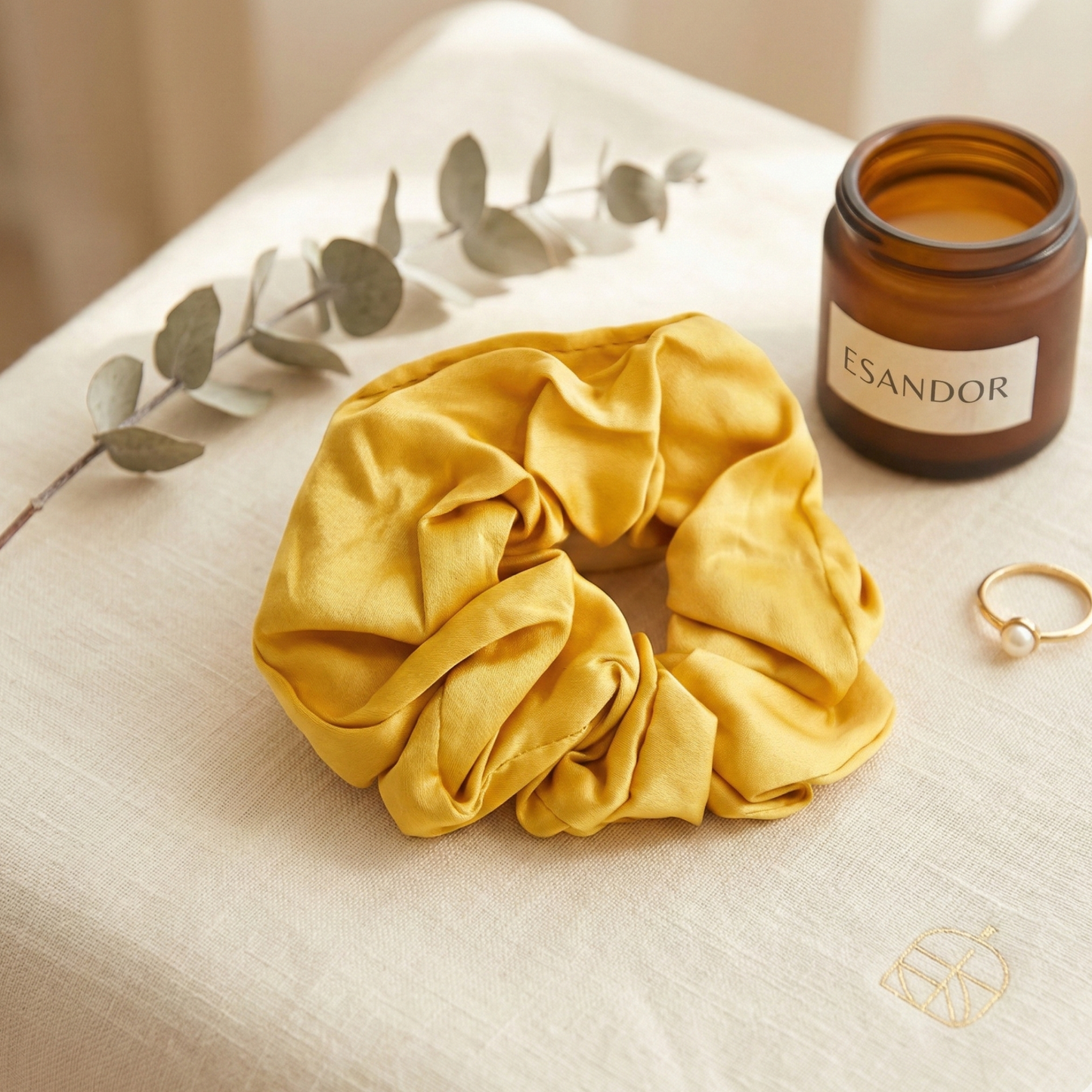 Yellow scrunchie on a textured surface with a candle and eucalyptus branch in the background.