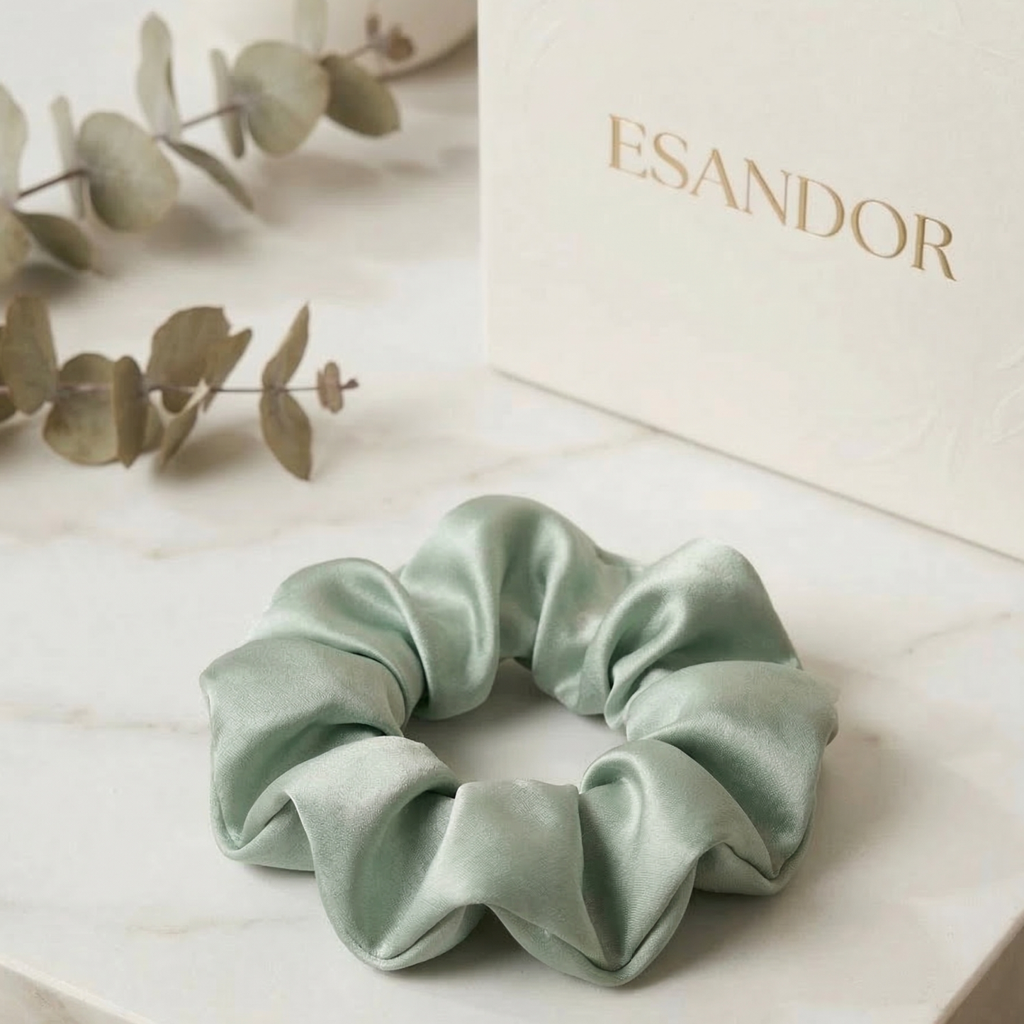 Light green scrunchie on a light surface with 'ESANDOR' branding in the background.