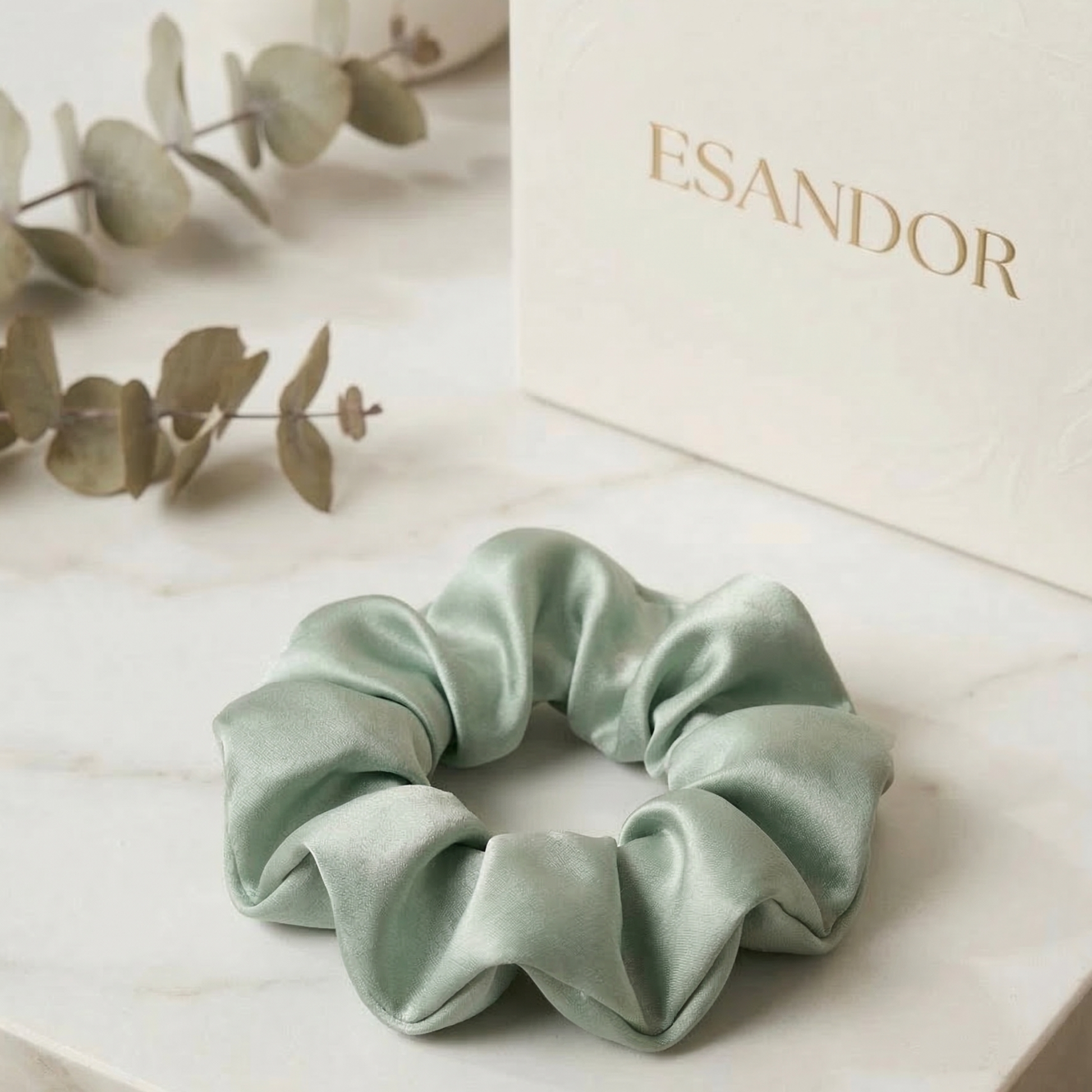 Light green scrunchie on a light surface with 'ESANDOR' branding in the background.